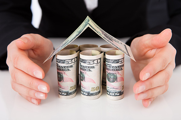 Pair of hands protecting a house made out of currency