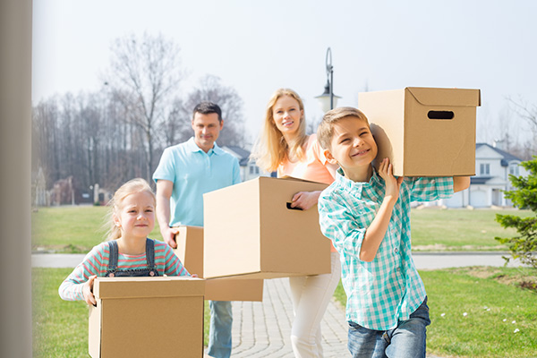 Mom, dad and two kids carrying boxes into their new home