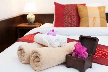 guest bedroom bed with decorative pillows, rolled up towels and a small gift