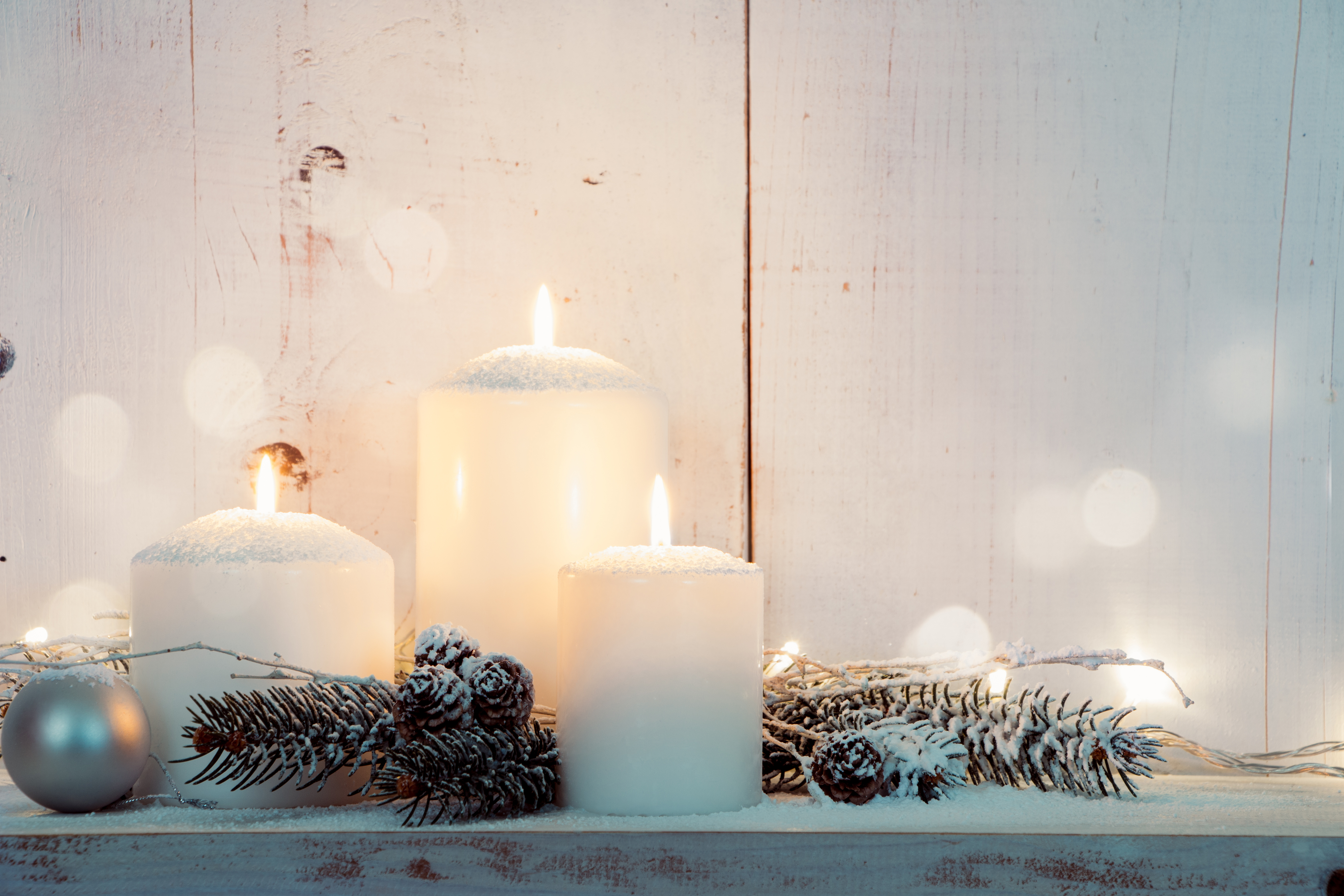 White pillar candles surrounded by snow covered pinecones